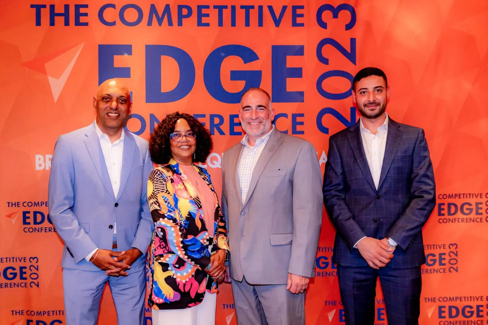 Four people standing in front of a sign that reads " competitive edge conference 2 0 1 3 ".