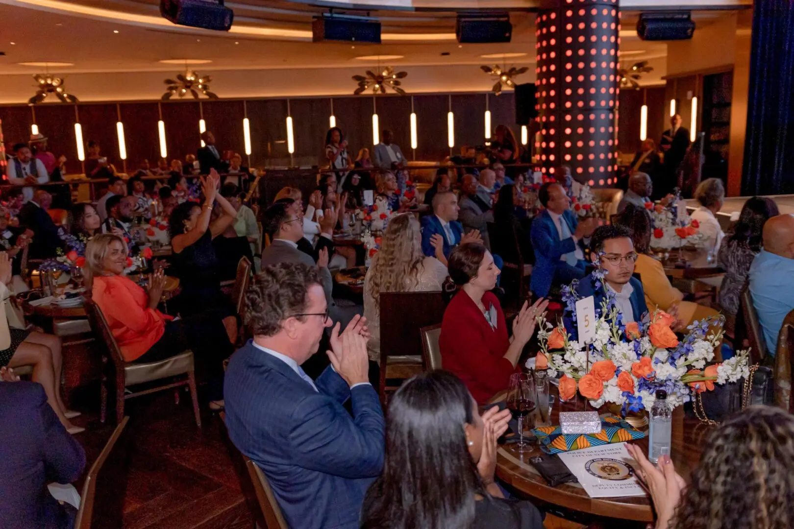 A crowd of people sitting at tables in front of a wall.