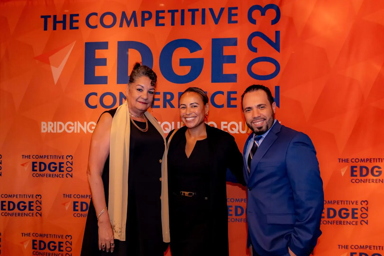 Three people standing in front of a sign for the competitive edge conference.