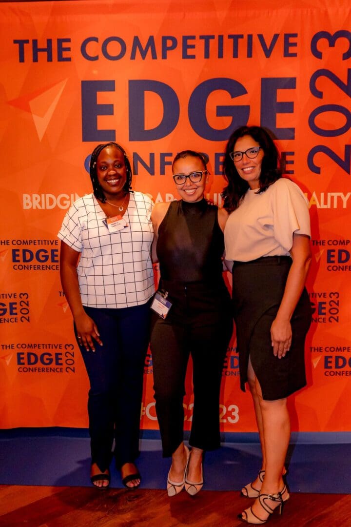 Three women standing in front of a orange wall.