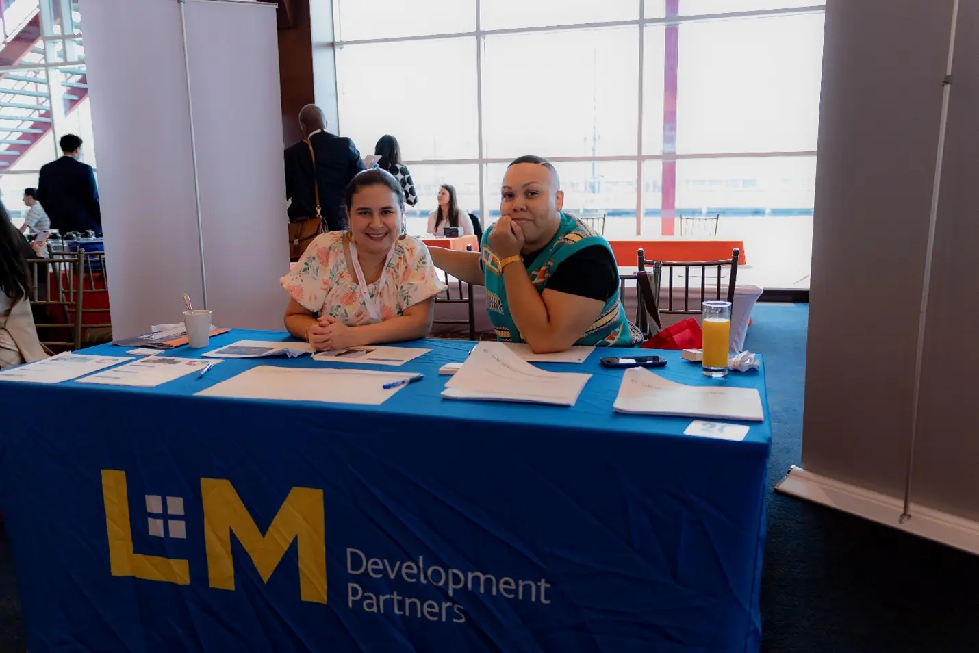 Two people sitting at a table with an event logo on it.